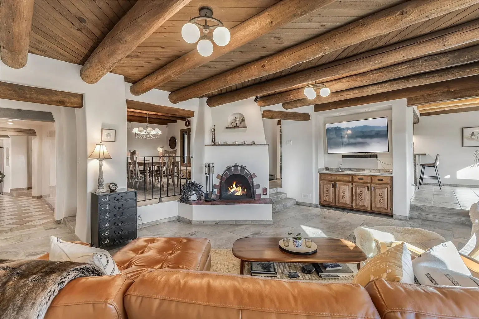 Cozy living room with wooden beams, fireplace, leather sofa, and wall-mounted TV.