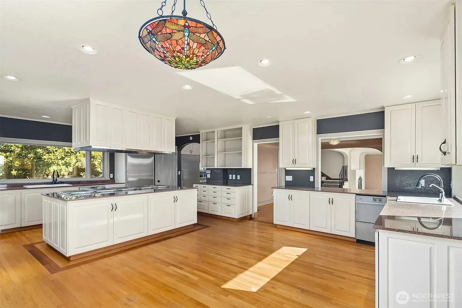 Spacious kitchen with white cabinets, hardwood floors, stainless steel appliances, and a colorful stained glass light fixture.