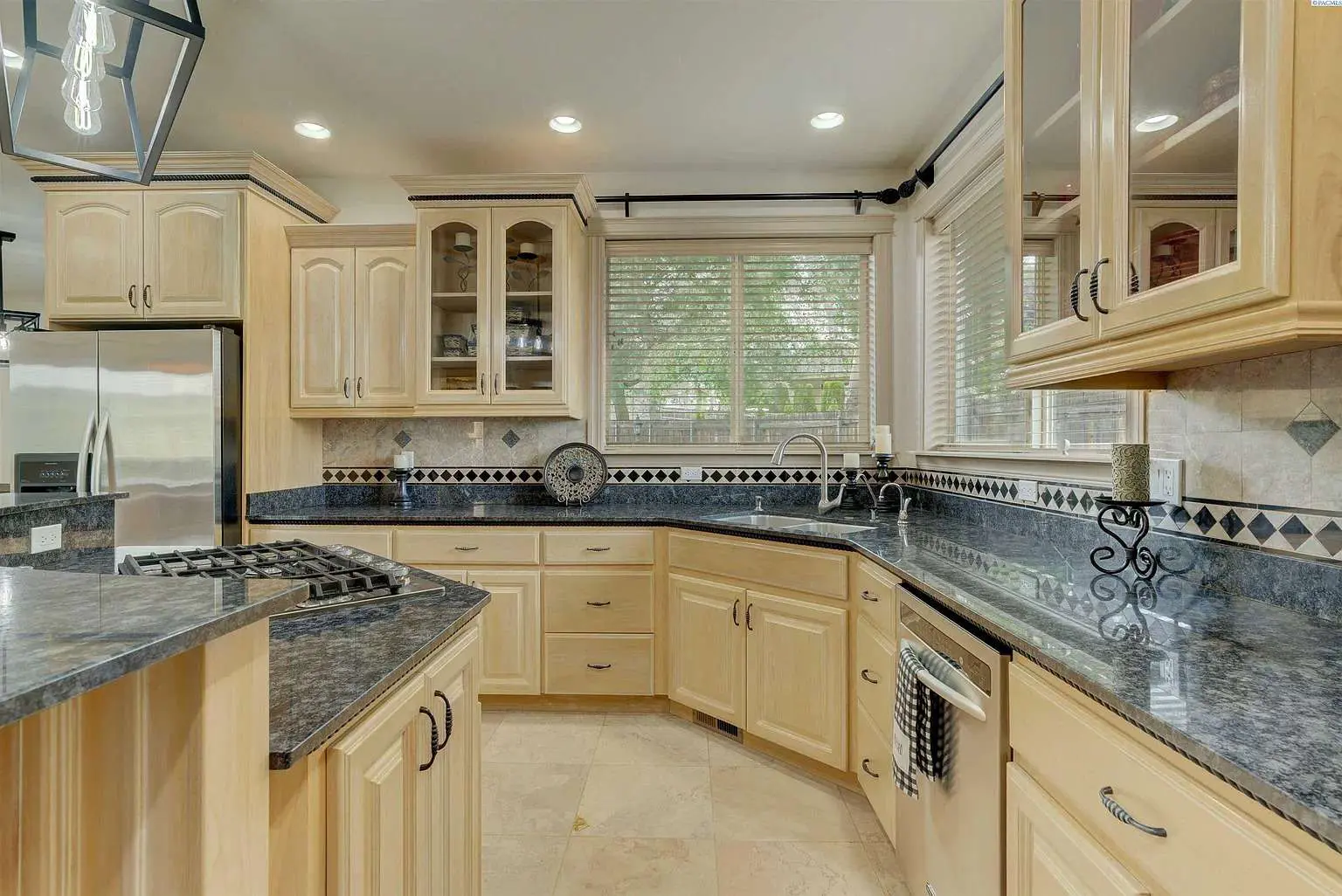 Spacious kitchen with light wood cabinets, dark countertops, stainless steel appliances, and large windows.
