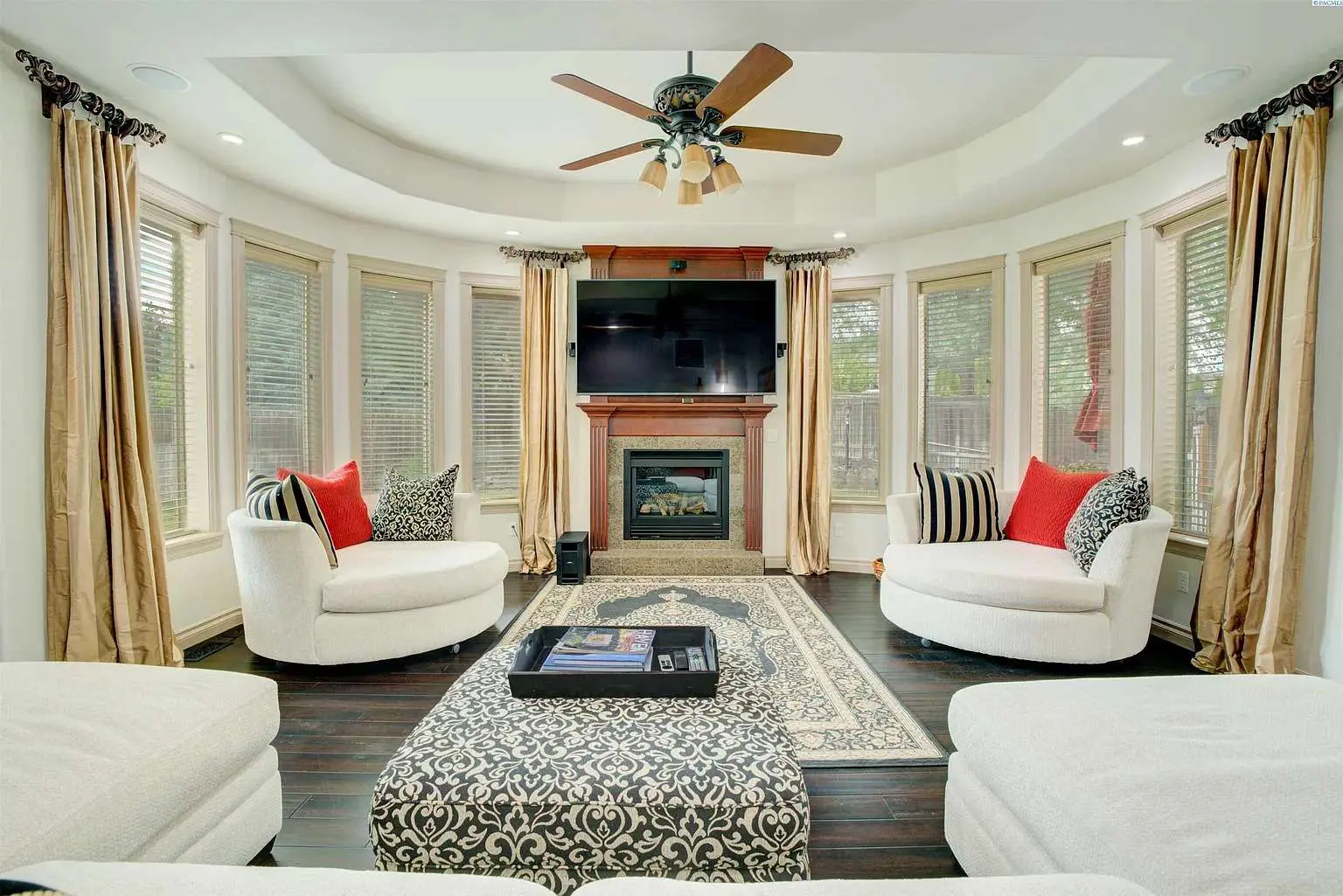 Spacious living room with circular sofas, fireplace, TV, and large windows with curtains.