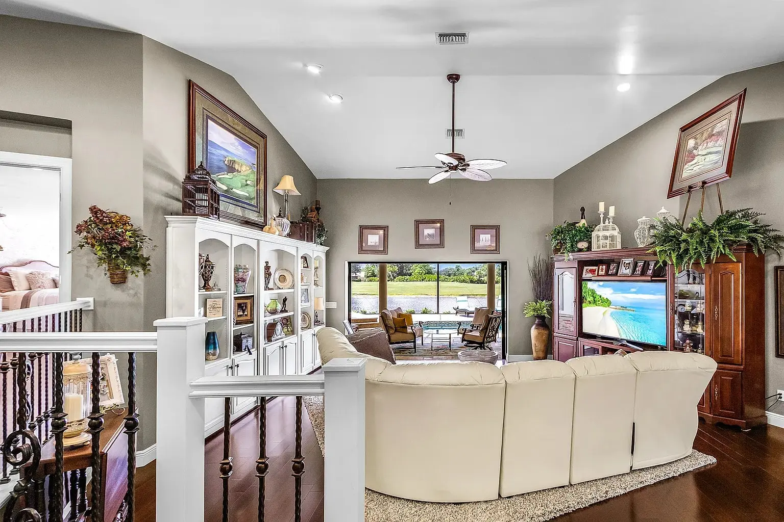 Spacious living room with white sectional sofa, large TV, and decorative shelves, overlooking a scenic view.
