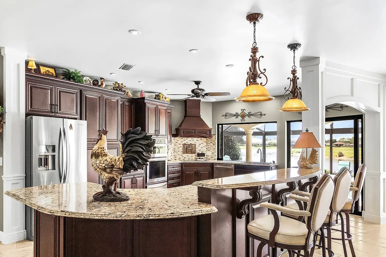 Spacious kitchen with dark wood cabinets, granite countertops, and bar seating, featuring decorative rooster statue.