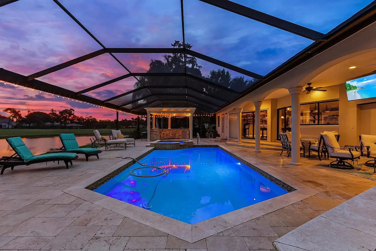 Outdoor pool area with lounge chairs, covered patio, and sunset sky in the background.
