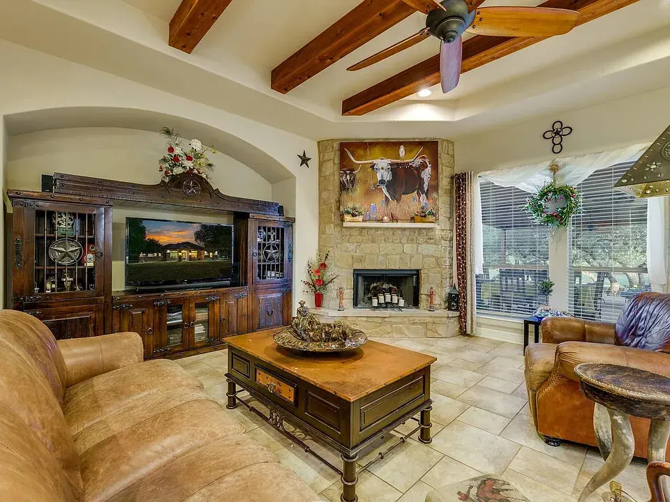 Rustic living room with leather furniture, wooden beams, stone fireplace, and large TV.