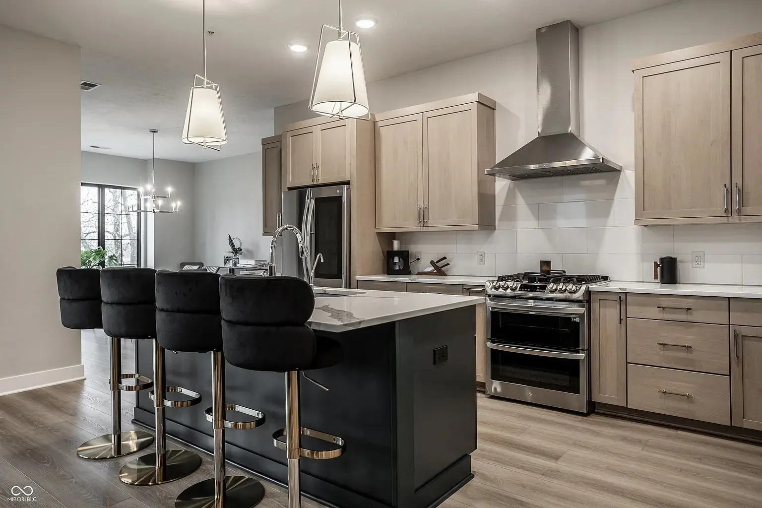 Modern kitchen with light wood cabinets, black island, stainless steel appliances, and three black bar stools.