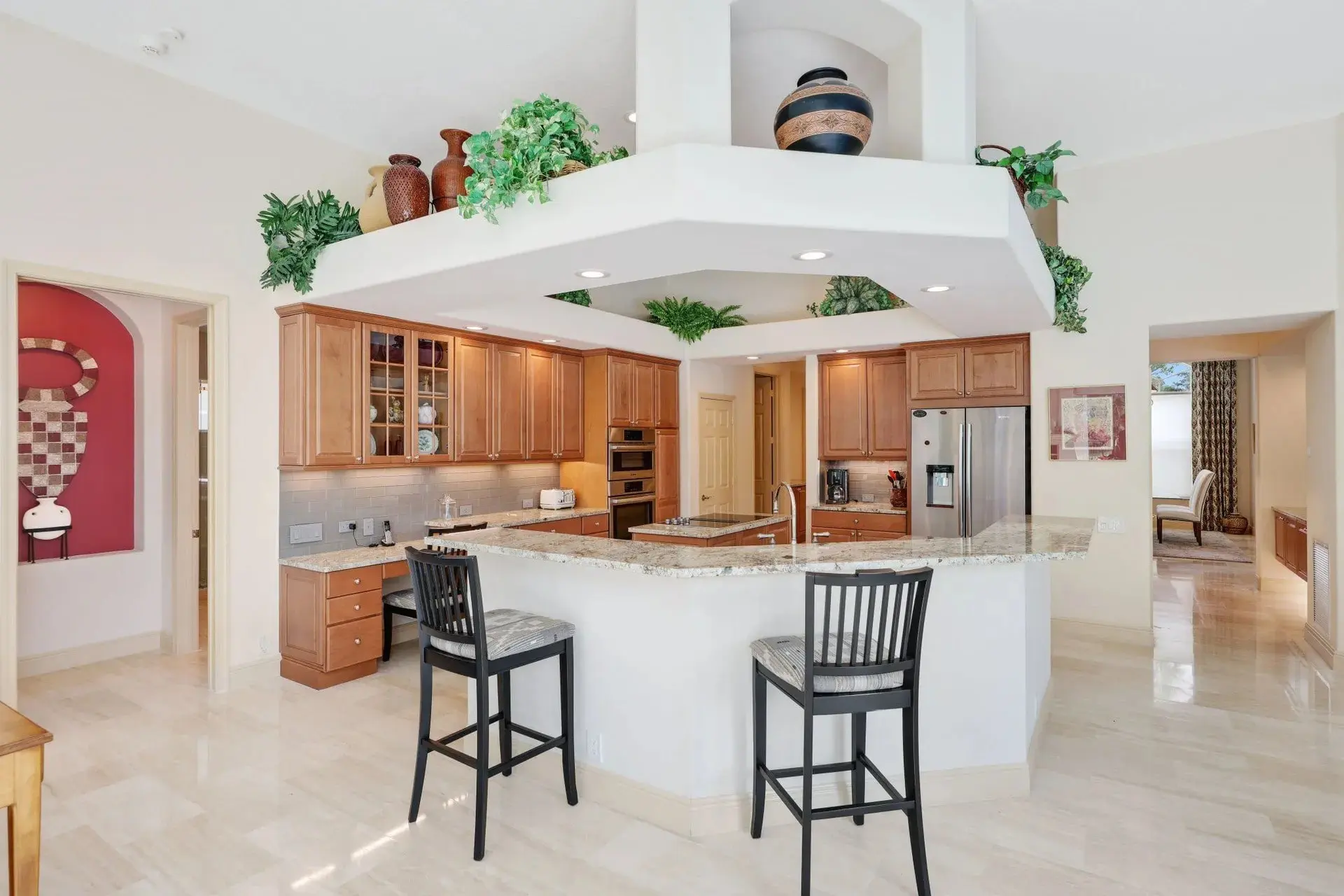 Spacious kitchen with wooden cabinets, granite countertops, bar stools, and decorative plants.