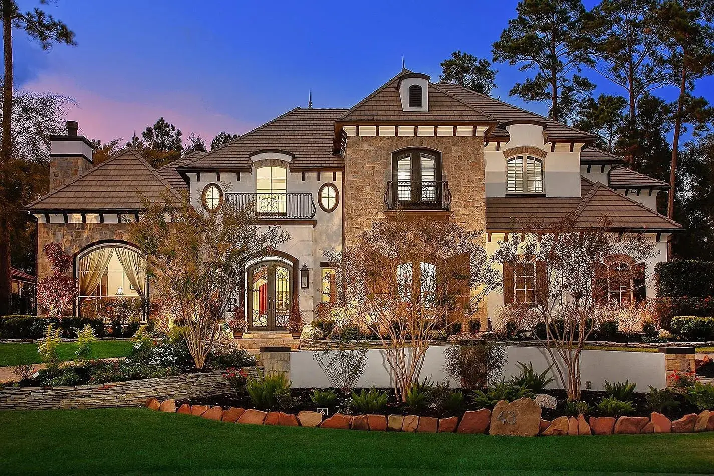 Elegant two-story house with stone facade, large windows, and landscaped garden at dusk.