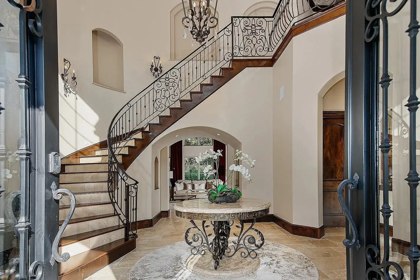 Elegant foyer with a curved staircase, ornate railing, and a central round table with orchids.
