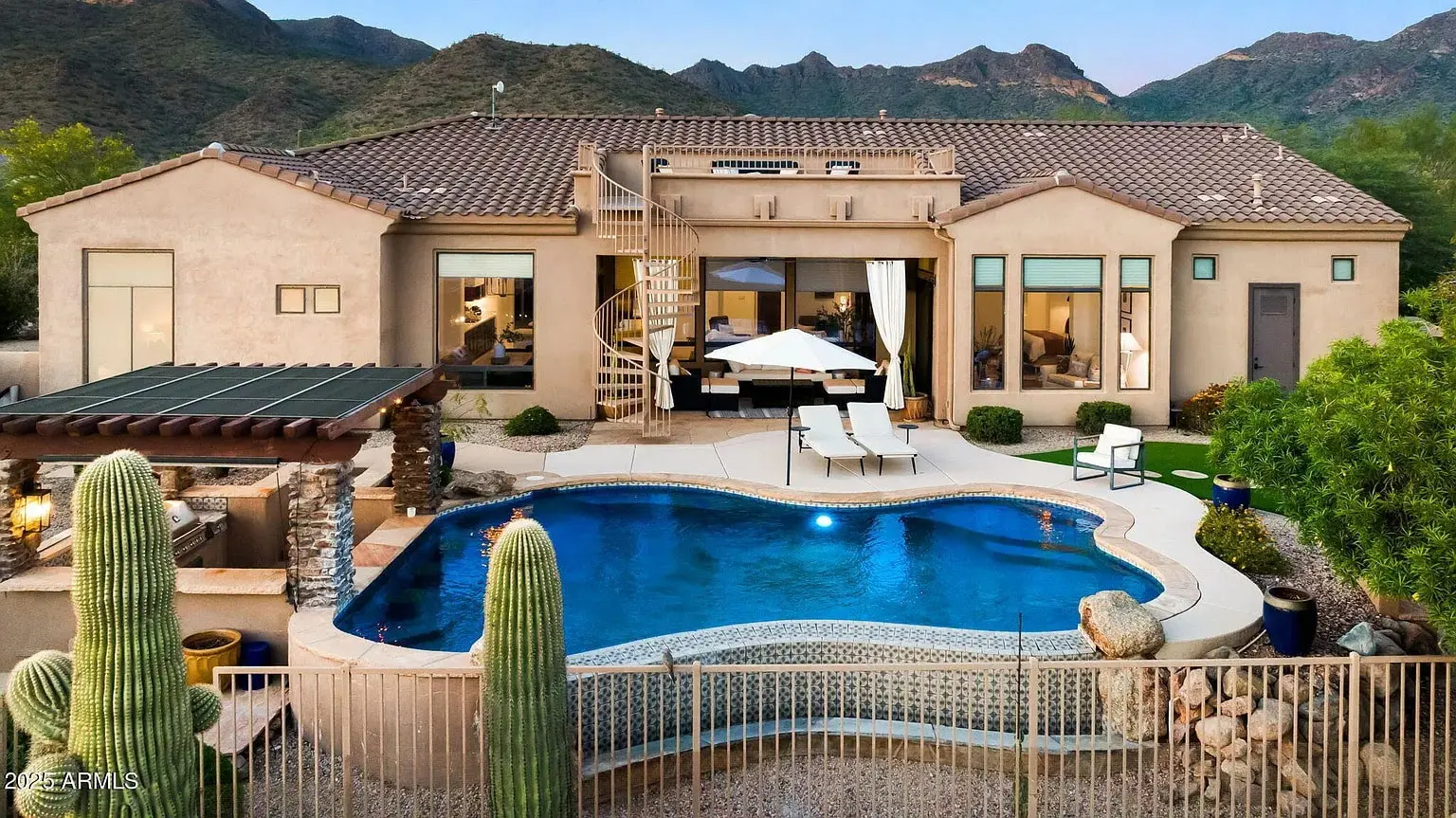 Luxury desert home with pool, spiral staircase, and mountain views in the background.