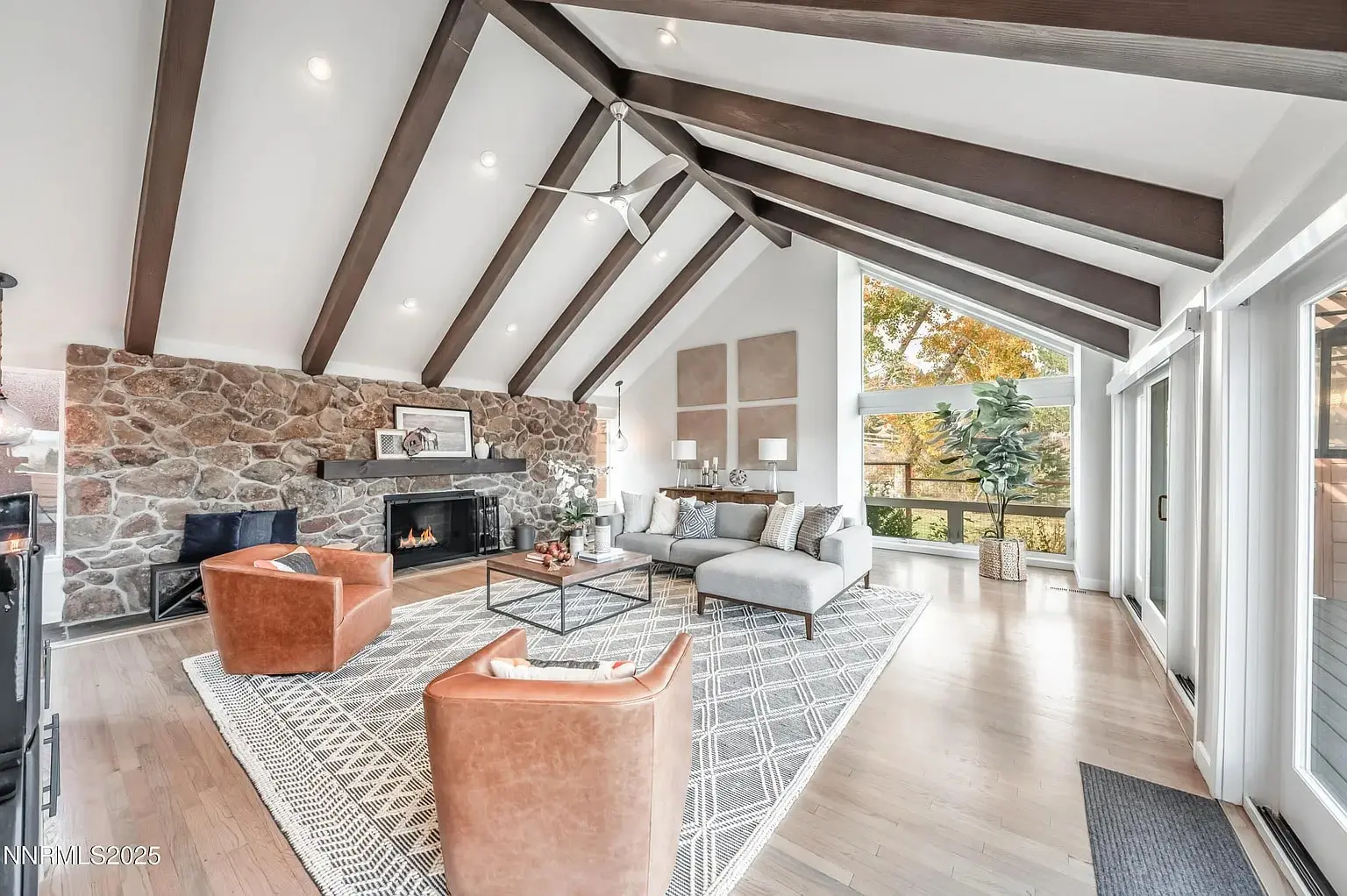 Spacious living room with vaulted ceiling, stone fireplace, large windows, and modern furniture.