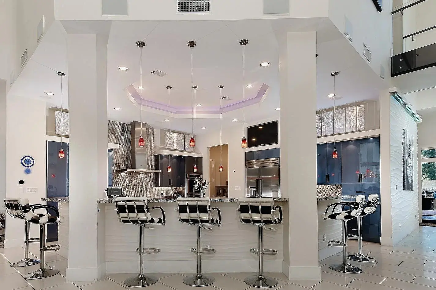 Modern kitchen with a central island, bar stools, pendant lights, and stainless steel appliances.