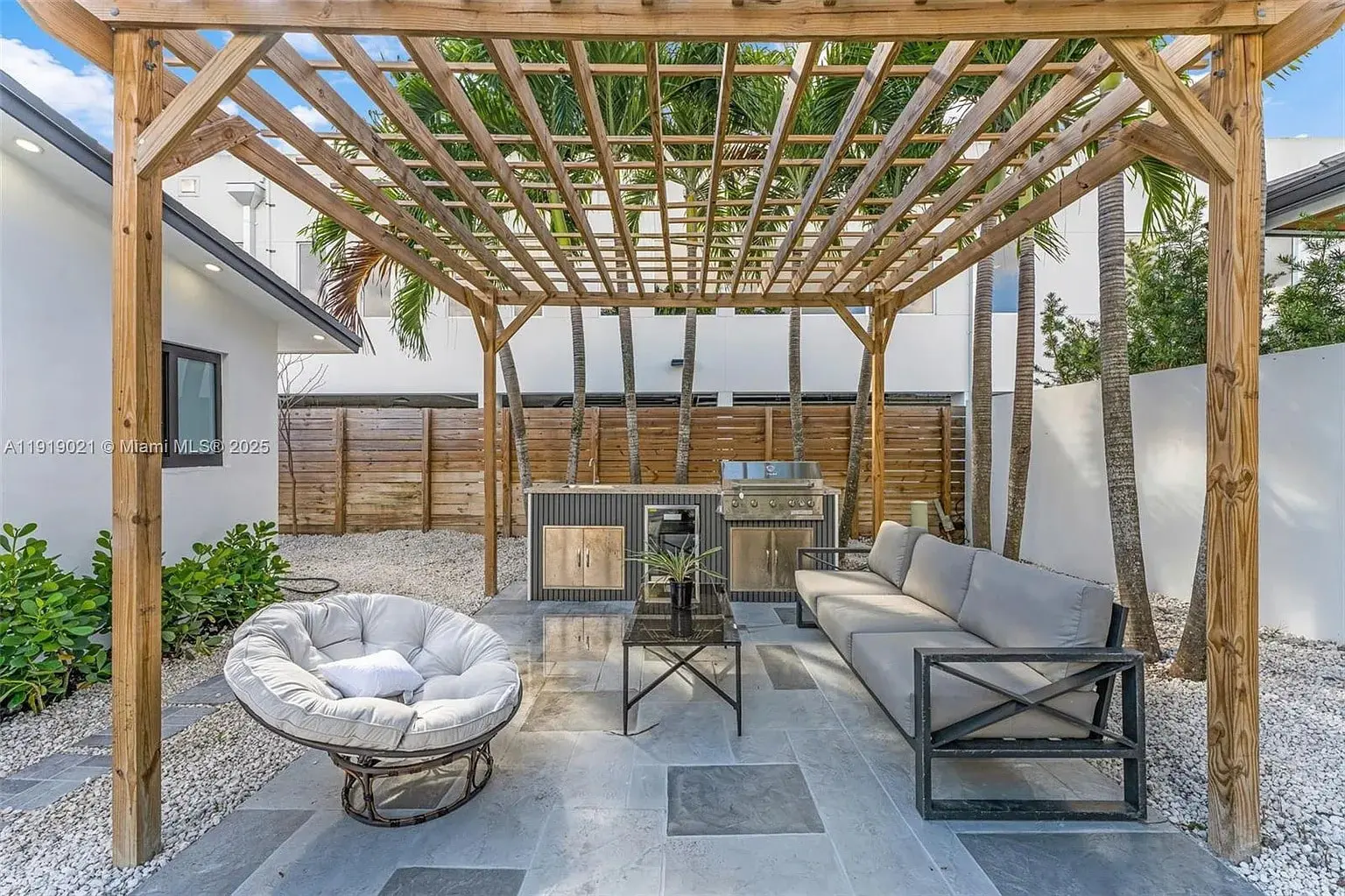 Outdoor patio with wooden pergola, modern seating, grill, and surrounding plants.
