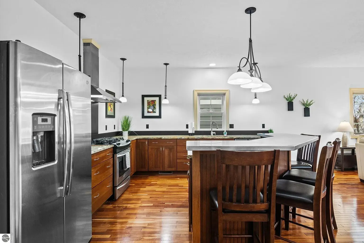 Modern kitchen with stainless steel appliances, wooden cabinets, island with chairs, and pendant lighting.