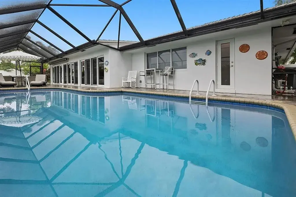 Indoor swimming pool with clear water, surrounded by a screened enclosure and patio furniture.