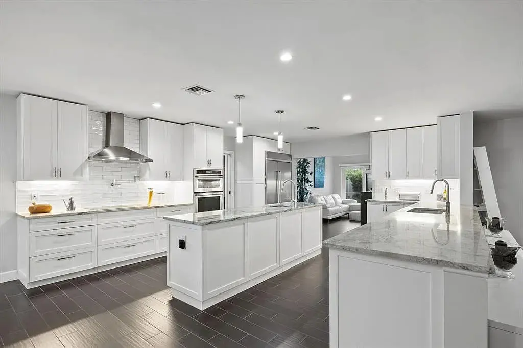 Modern kitchen with white cabinets, marble countertops, stainless steel appliances, and dark wood flooring.