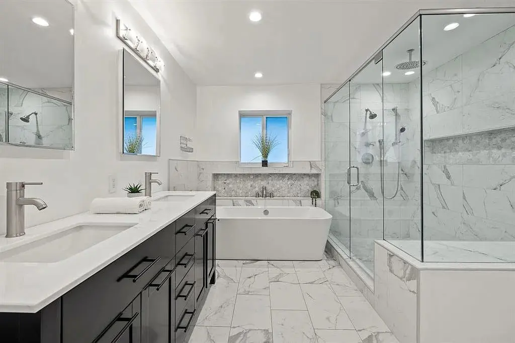 Modern bathroom with marble tiles, double vanity, freestanding tub, and glass-enclosed shower.