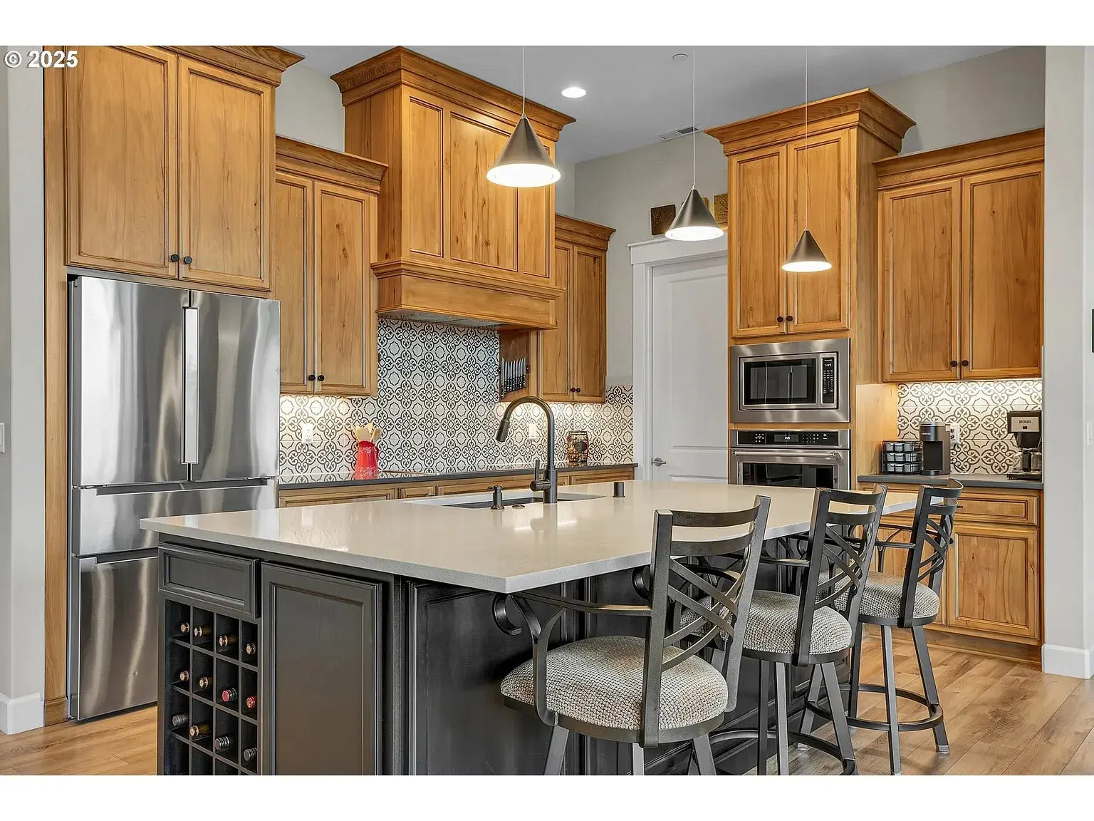 Modern kitchen with wooden cabinets, island with bar stools, stainless steel appliances, and patterned backsplash.