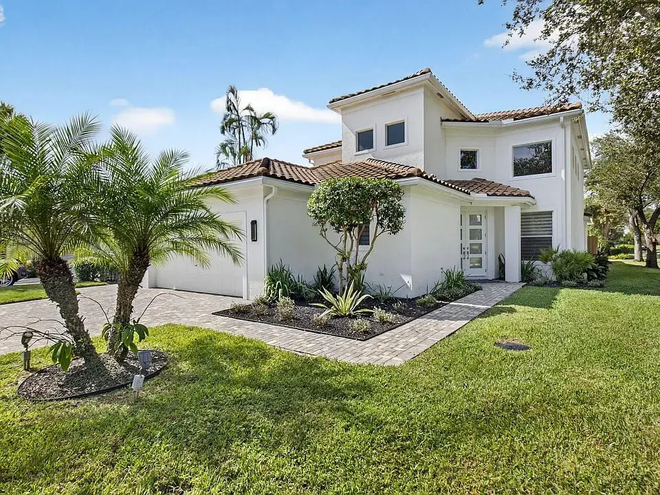 Modern two-story white house with a tiled roof, surrounded by palm trees and a manicured lawn.