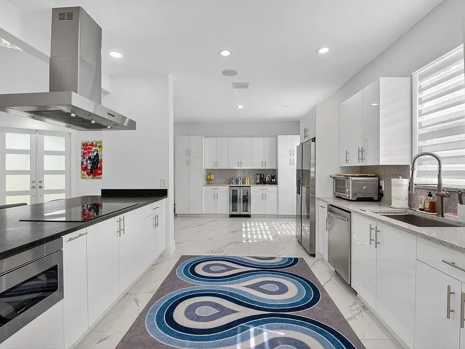 Modern kitchen with white cabinets, stainless steel appliances, and a patterned rug on the floor.