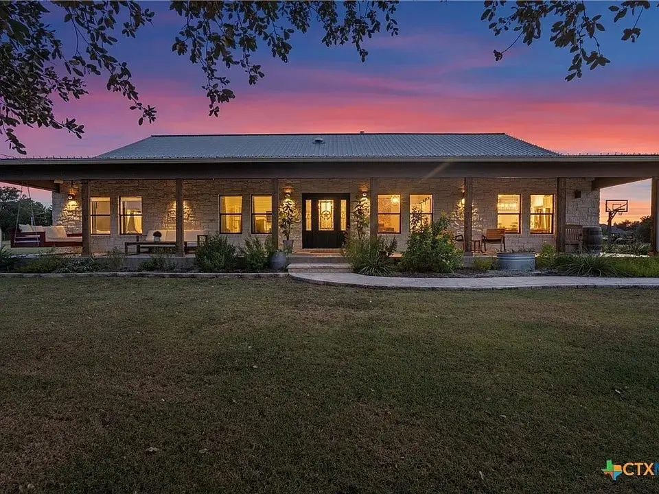 Single-story house with large windows, lit warmly at sunset, surrounded by a grassy yard.