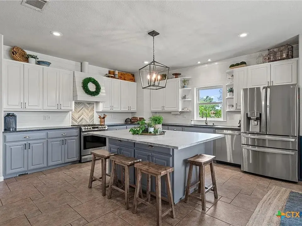 Modern kitchen with gray and white cabinets, large island, and stainless steel appliances.