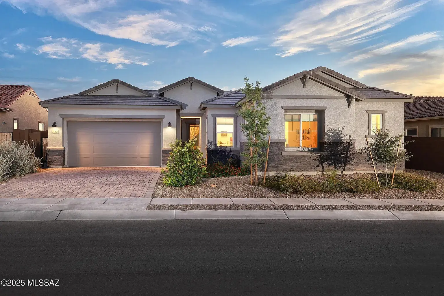 Single-story modern house with a two-car garage, illuminated at dusk.