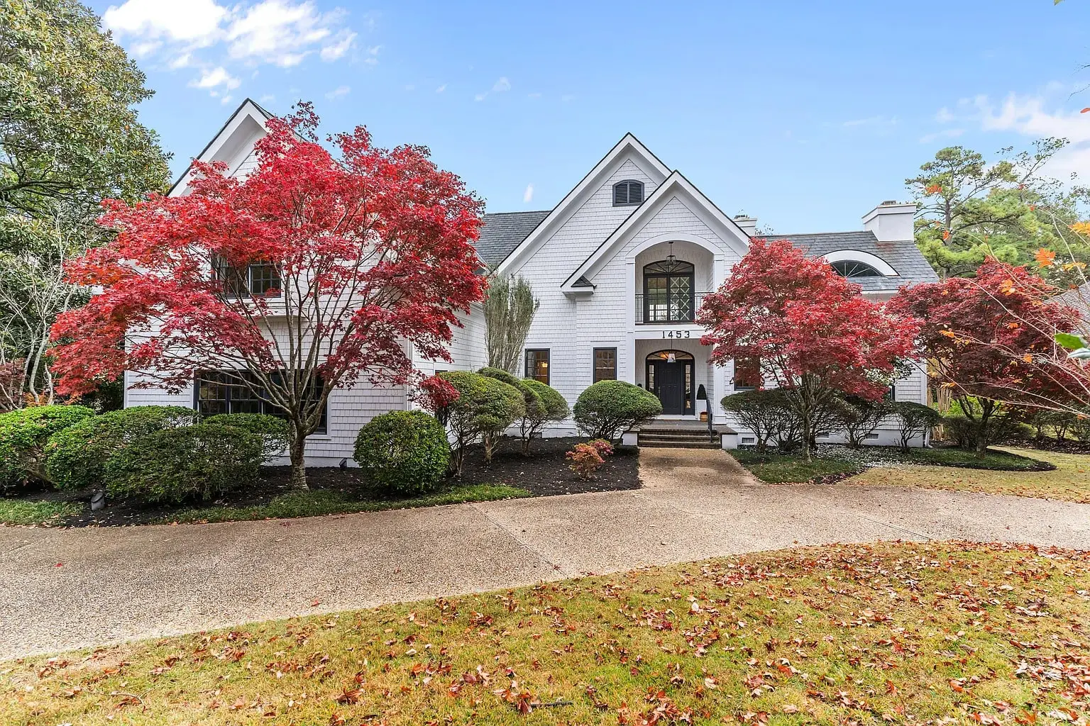 White house with peaked roof, surrounded by red-leaved trees and shrubs, on a clear day.