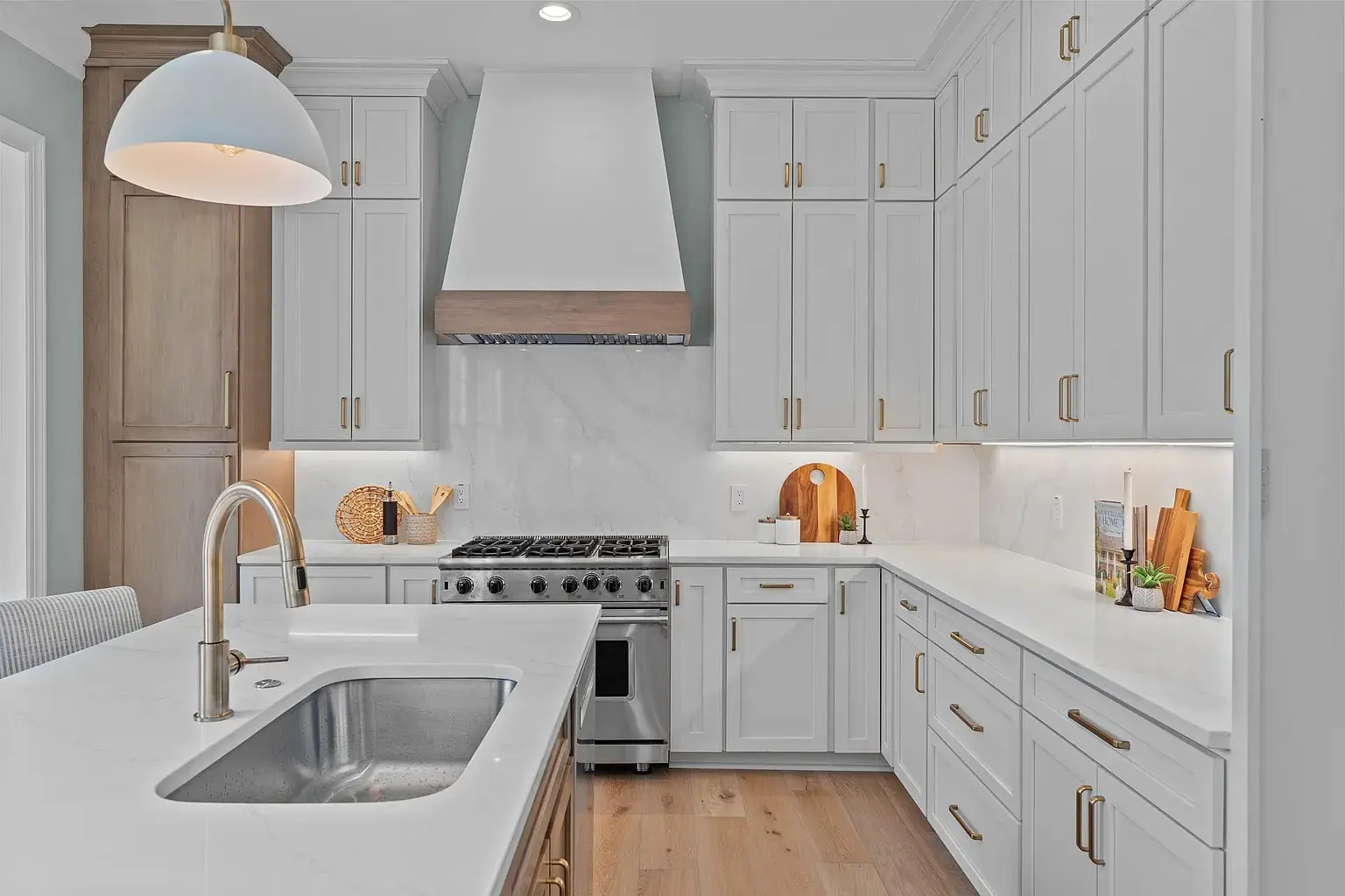 Modern kitchen with white cabinets, marble countertops, stainless steel appliances, and wooden floor.