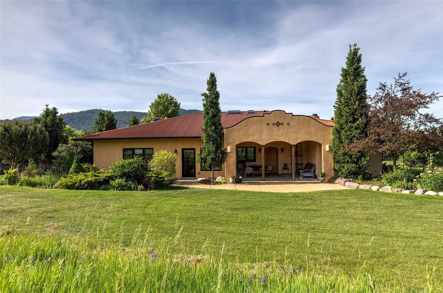 Single-story house with a red roof, surrounded by lush greenery and a well-maintained lawn.