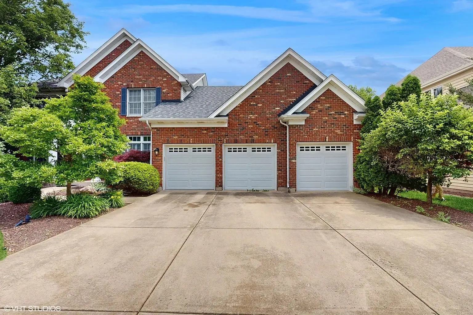 Brick house with three-car garage, gabled roof, and surrounding greenery.