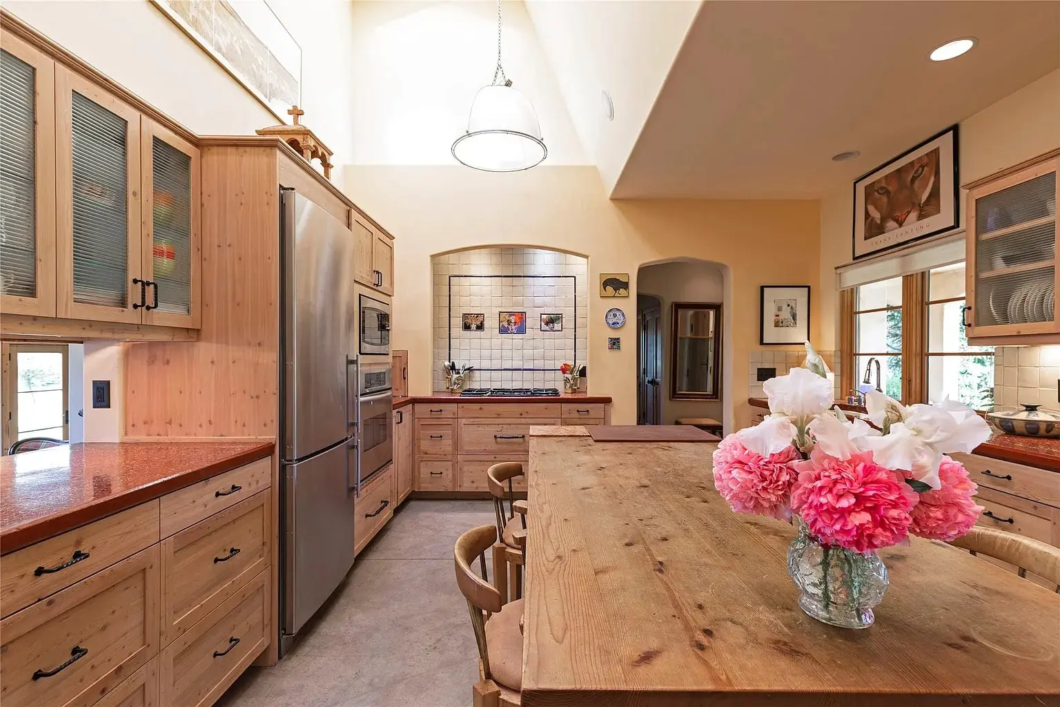 Spacious kitchen with wooden cabinets, large island, stainless steel appliances, and a vase of pink flowers.