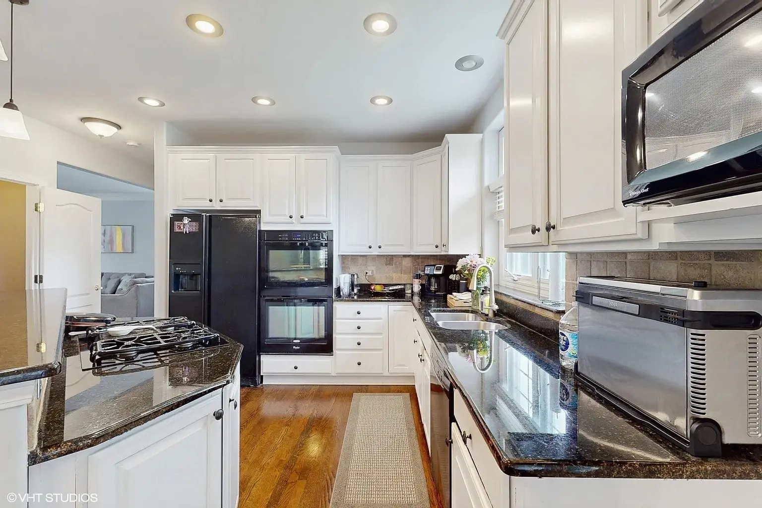 Modern kitchen with white cabinets, black appliances, granite countertops, and wooden flooring.
