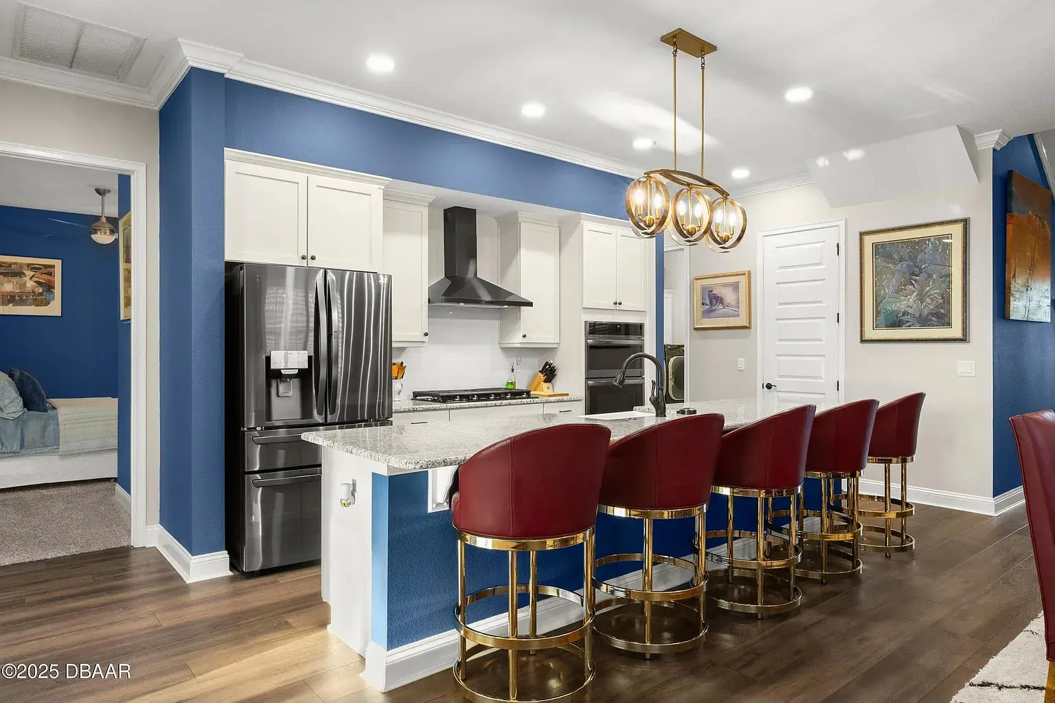 Modern kitchen with blue walls, white cabinets, stainless steel appliances, and red barstools at a marble island.