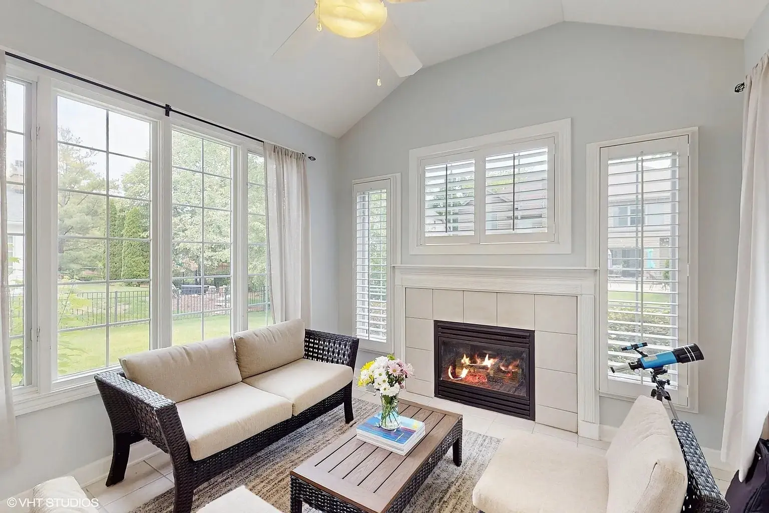 Bright sunroom with wicker furniture, fireplace, large windows, and a telescope.