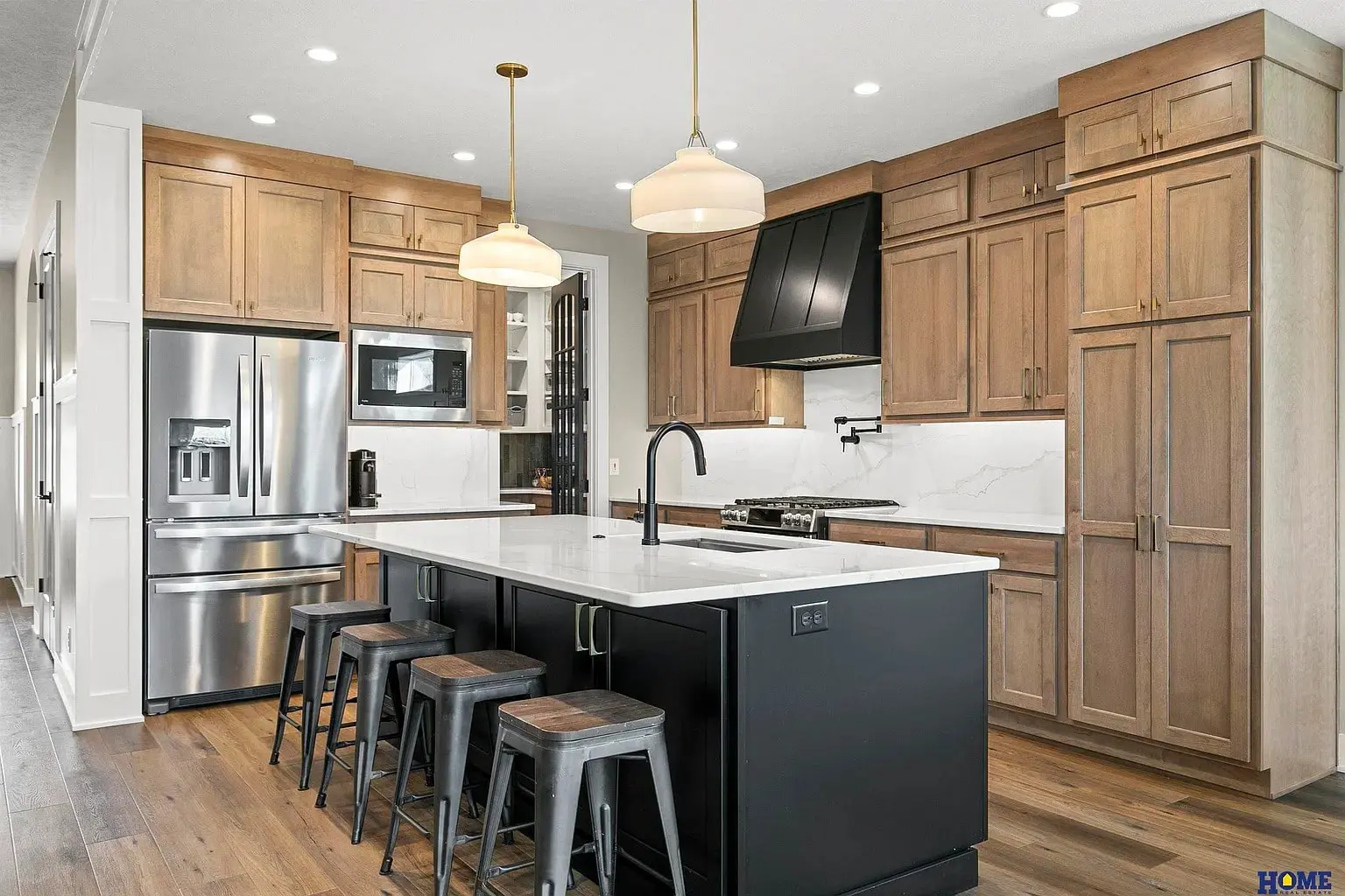 Modern kitchen with wooden cabinets, black island, stainless steel appliances, and bar stools.