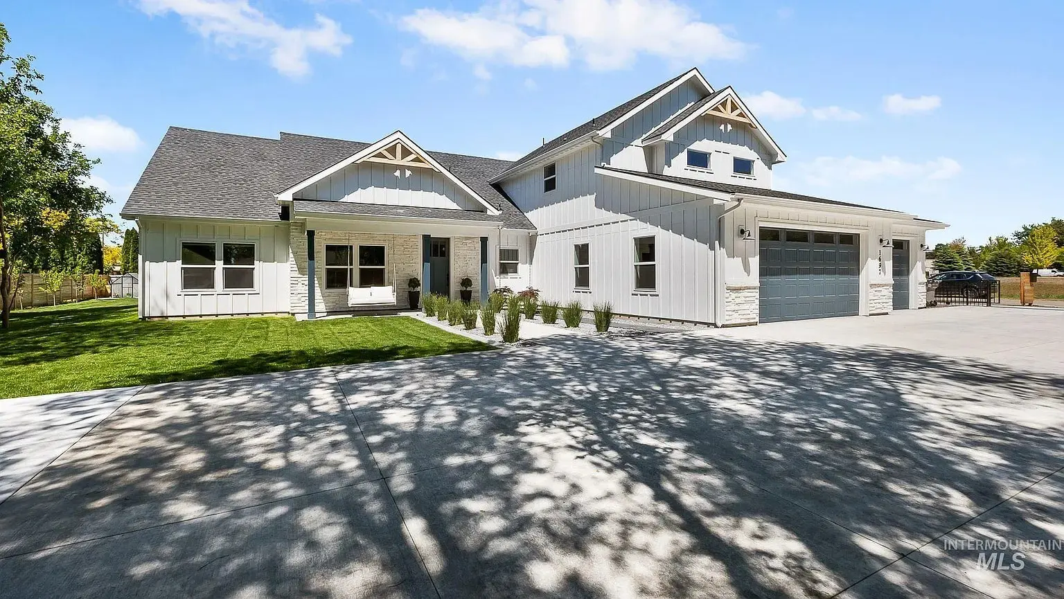 Modern white house with a large driveway, two-car garage, and surrounding greenery under a blue sky.