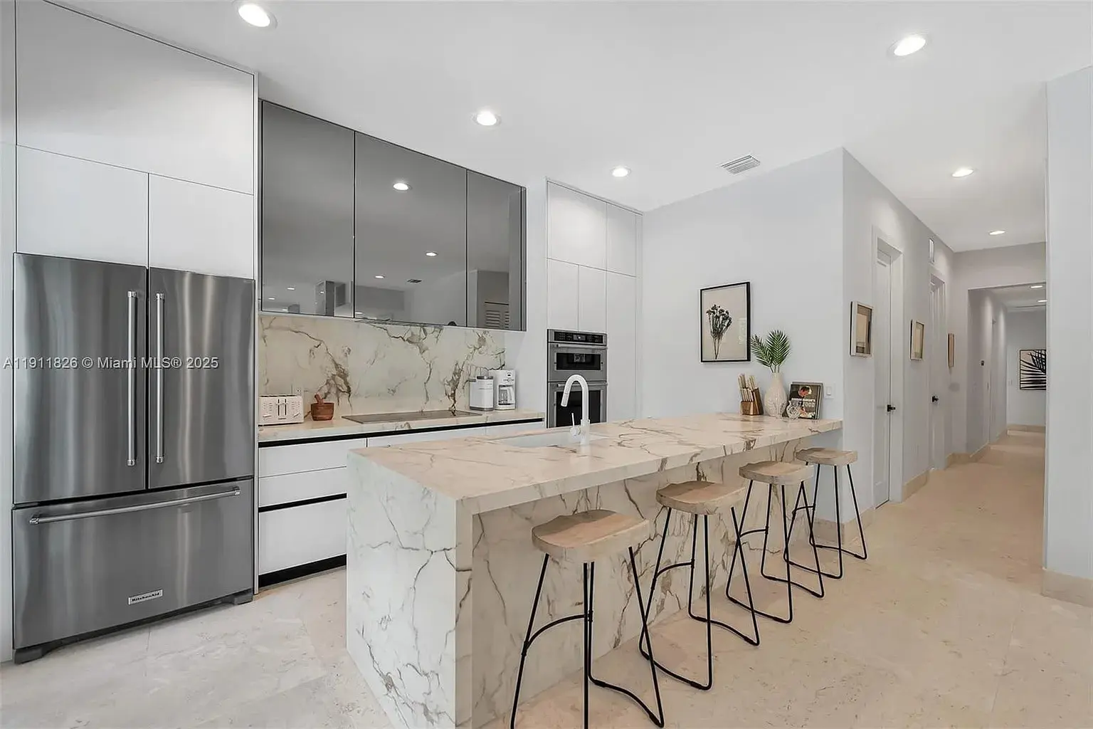 Modern kitchen with marble countertops, stainless steel appliances, and four wooden bar stools at the island.