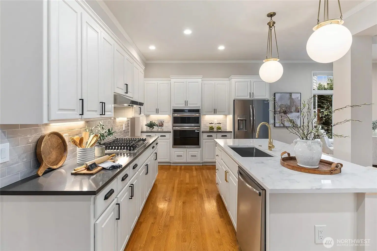Modern kitchen with white cabinets, stainless steel appliances, marble countertops, and wooden flooring.