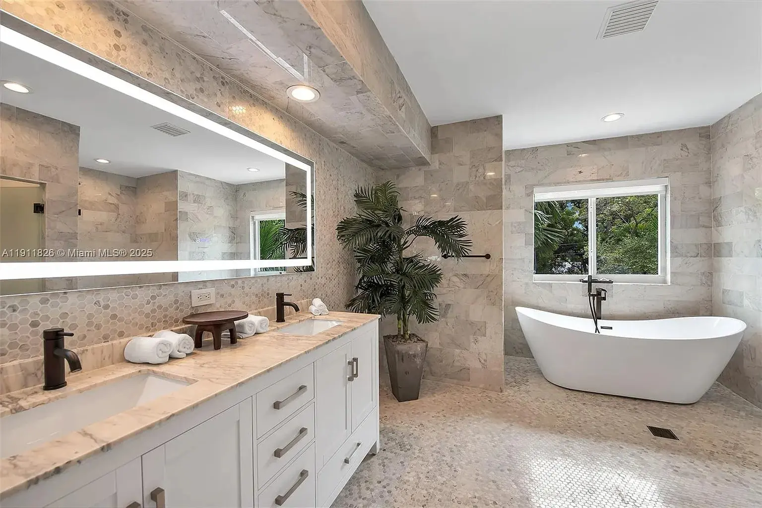 Modern bathroom with freestanding tub, double sink vanity, large mirror, and decorative plants.