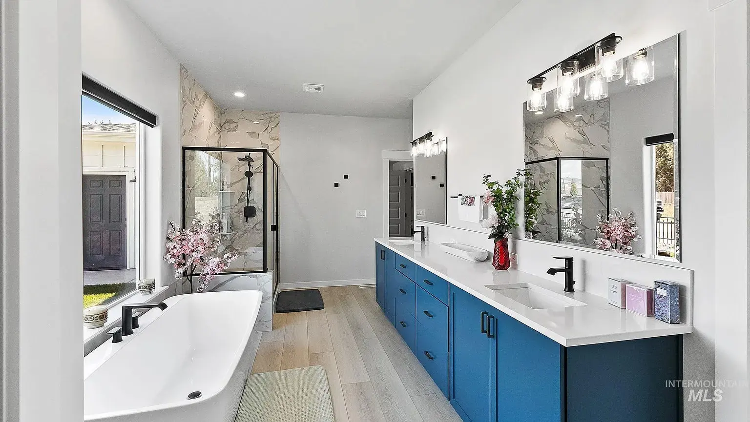 Modern bathroom with blue double vanity, freestanding bathtub, and glass-enclosed shower.