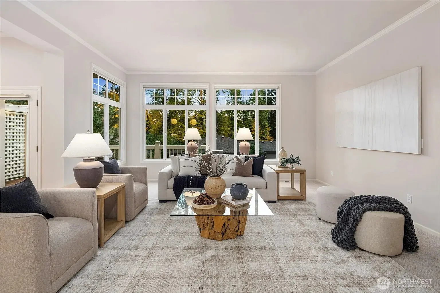 Modern living room with large windows, neutral tones, cozy seating, and a wooden coffee table.