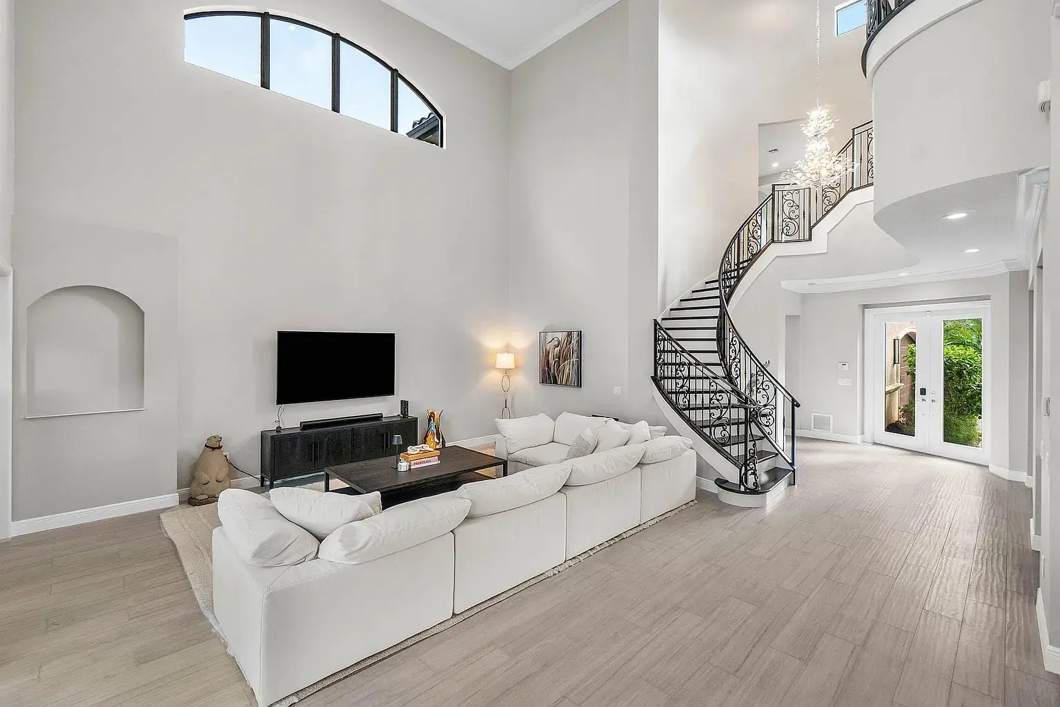 Spacious living room with white sectional sofa, TV, and elegant spiral staircase.