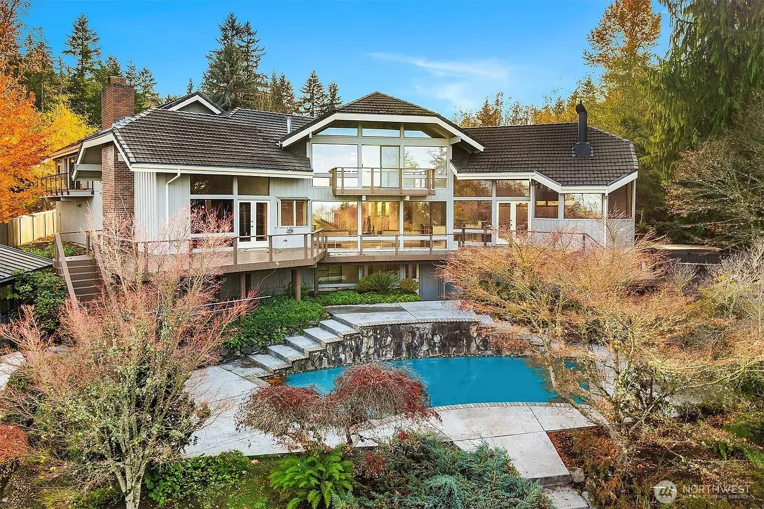 Modern two-story house with large windows, surrounded by trees, featuring a pool in the backyard.