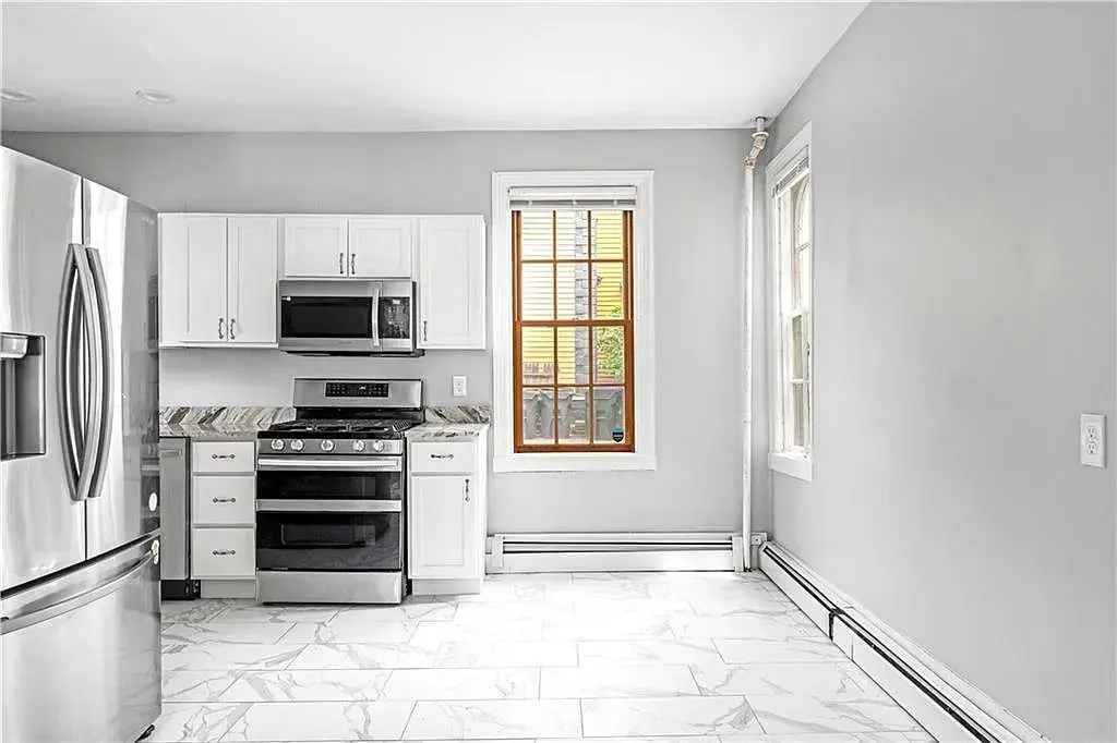 Modern kitchen with stainless steel appliances, white cabinets, and marble-patterned floor tiles.