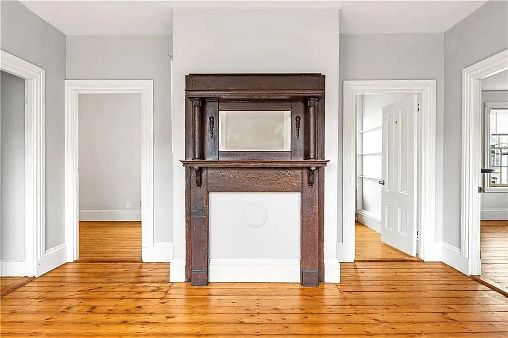 Room with wooden floors, a dark wooden fireplace, and three doorways.