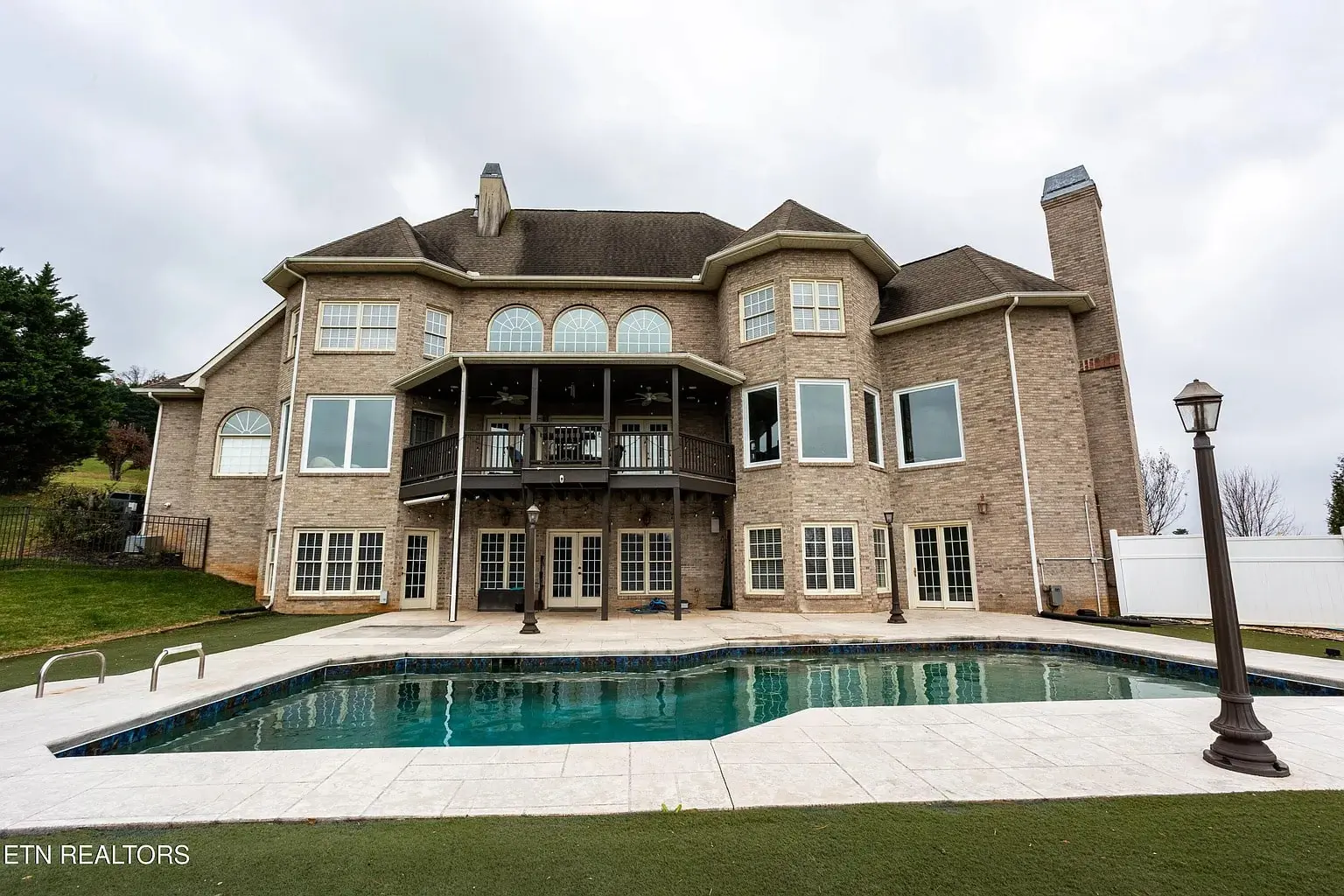 Large brick house with multiple windows, a balcony, and a swimming pool in the backyard.