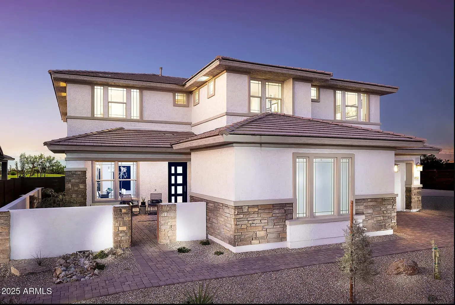 Modern two-story house with stone accents, large windows, and a small front yard at dusk.