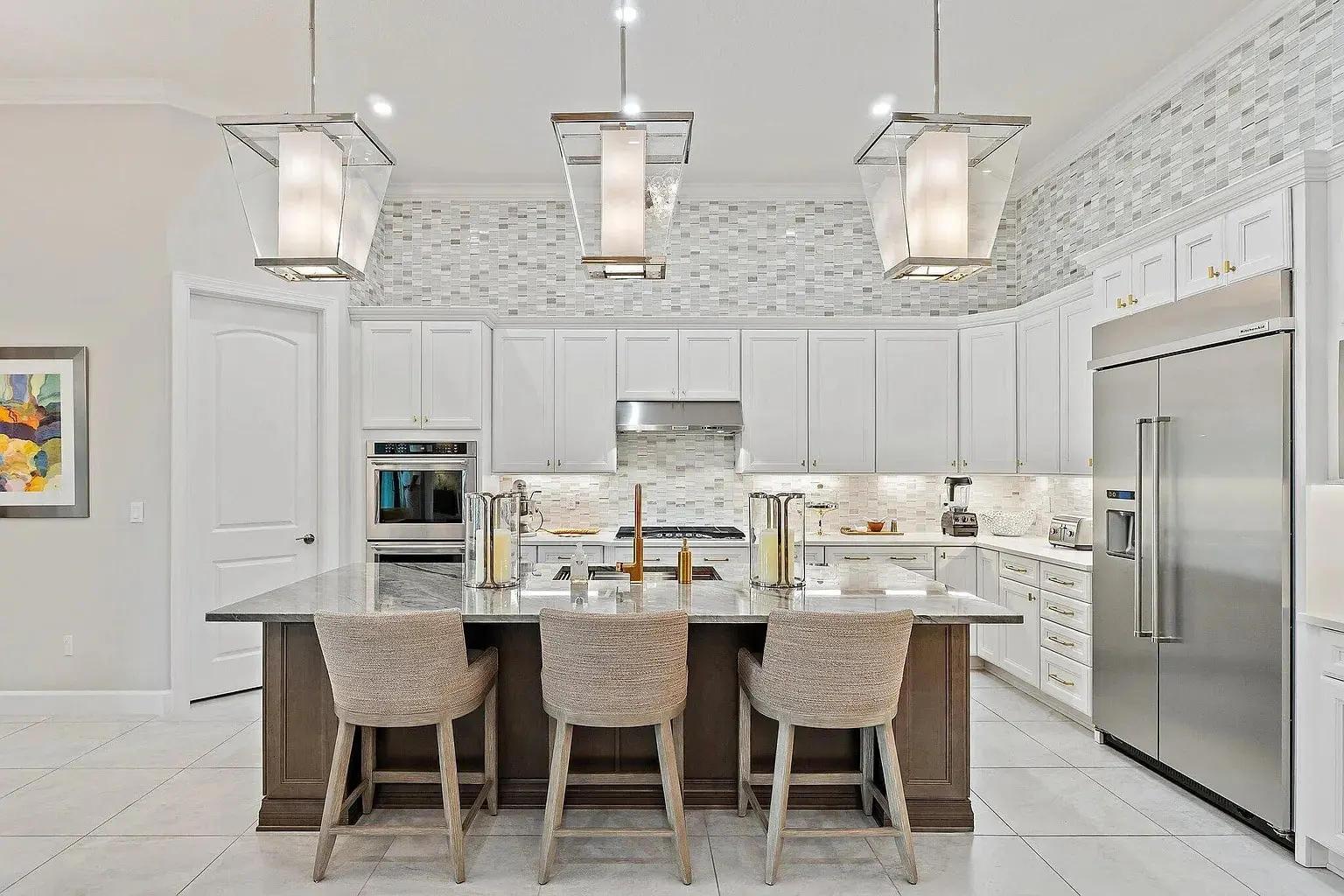 Modern kitchen with white cabinets, large island, three chairs, and stainless steel appliances.