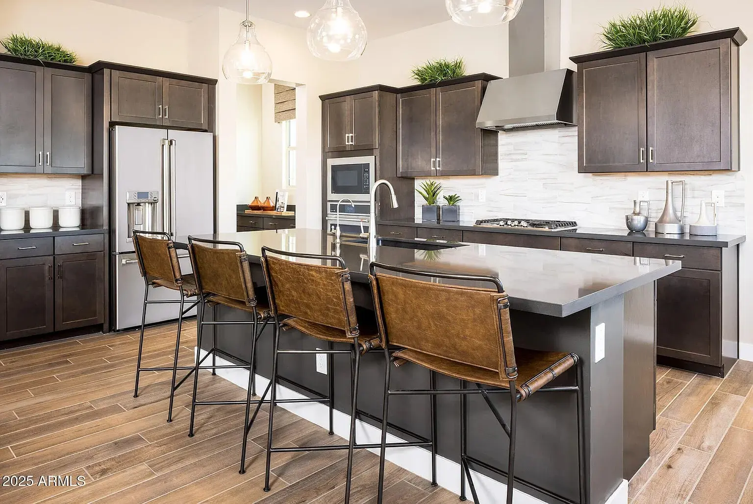 Modern kitchen with dark wood cabinets, island with bar stools, stainless steel appliances, and pendant lights.