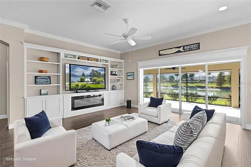 Modern living room with white furniture, large TV, and sliding glass doors overlooking a scenic view.